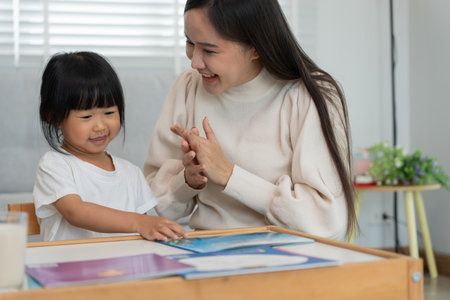 Happy Asian mother relax and read book with baby time together at home. parent sit on sofa with daughter and reading a story. learn development, childcare, laughing, educationの写真素材
