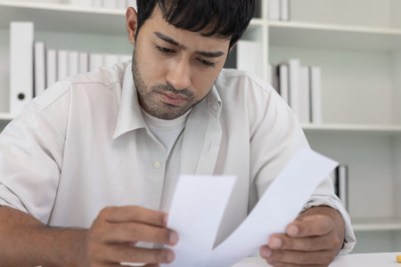Stressed and headache asian man with large bills or invoices no money to pay to expenses and credit...
