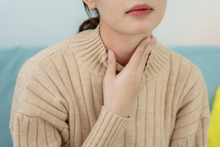 Asian woman put on neck due to a sore throat. female tonsillitis causes a inflammation. treated by taking water, taking antibiotics, consult a doctor, virus, corona virusの写真素材