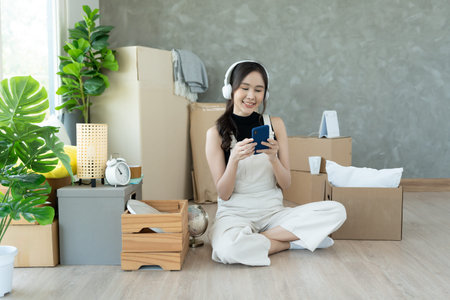 Moving house, relocation. asian woman feel good and recreation and use phone on new house, inside...