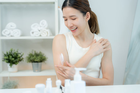 Beautiful Asian woman smiling while applying cream for good skin. Healthy woman applying cream for body.の写真素材