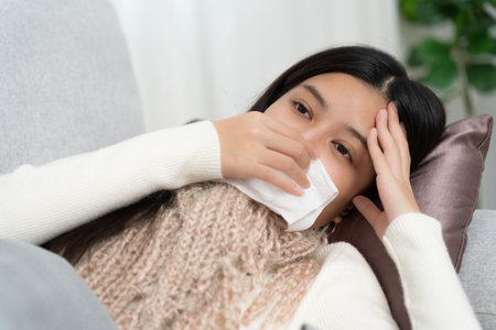 sick woman with a headache sitting under blanket, female sneezing and runny nose with seasonal influenza, allergic, high fever and influenza, resting, virus, coronavirusの写真素材