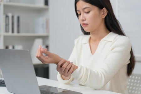 Asian young woman working in office with a carpal tunnel syndrome or wrist joint inflammation, hand muscle inflammation from office syndrome , hand muscle pain from workingの写真素材