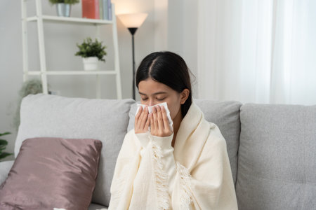 sick woman with a headache sitting under blanket, female sneezing and runny nose with seasonal influenza, allergic, high fever and influenza, resting, virus, coronavirusの写真素材