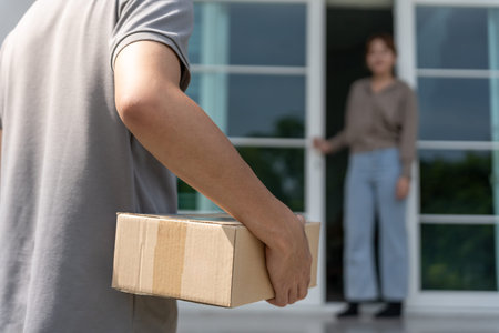 Happy smiling woman receives boxes parcel from courier in front house. Delivery man send deliver express. online shopping, paper containers, takeaway, postman, delivery serviceの写真素材