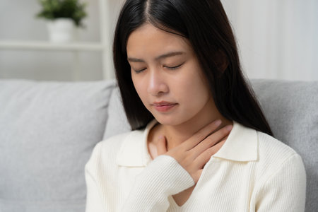 Asian woman put on neck due to a sore throat. female tonsillitis causes a inflammation. treated by taking water, taking antibiotics, consult a doctor, virus,の写真素材