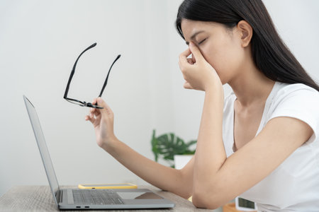 Eye problems, Asian women with tired and irritated eyes, eye rubbing, dry, eye pain after work, migraine, headache, blurred vision, photophobia, working in the dark,の写真素材
