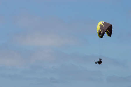 para glider with a black and yellow parachute flying in a blue sky with thin clouds の写真素材