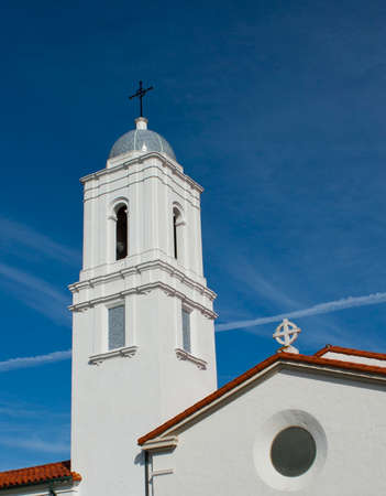 white stucco church with bell tower that has a blue tile top. red tile roof, blue sky with small clouds. crosses の写真素材