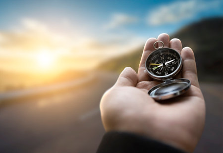 Traveler explorer man holding compass in a hand in mountains at sunrise, point of view.の写真素材