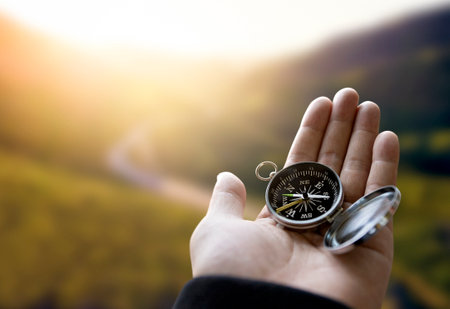 Traveler explorer man holding compass in a hand in mountains at sunrise, point of view.の写真素材