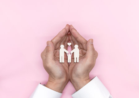 A man holding his hand in the family's paper silhouette on a bright pink backgroundの写真素材