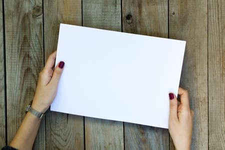 Woman holding blank paper on wooden table.