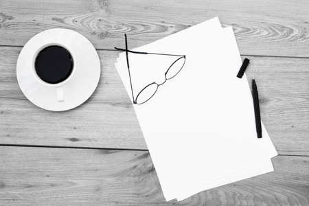 Blank white papers, coffee cup, eyeglasses and pen on wooden background.の写真素材