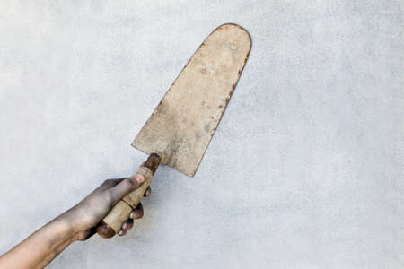 Hand holding a plaster trowel on gray background.の写真素材