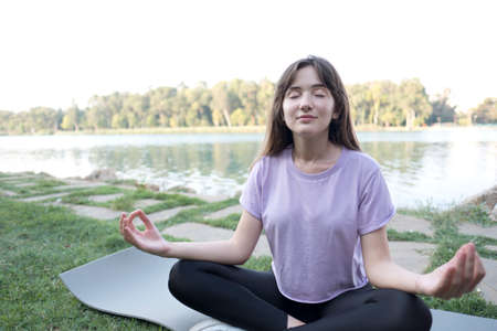 Young beautiful woman doing yoga exercises in park on the bank river.の写真素材