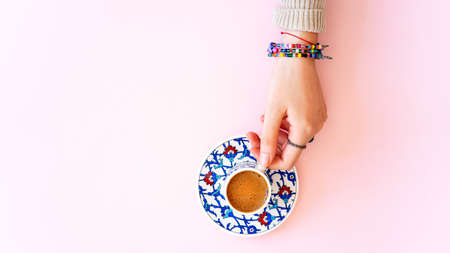 Woman hand holding a cup of Turkish coffee on pink backgroundの写真素材