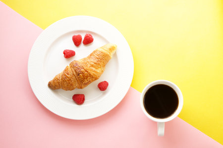 Coffee cup and fresh croissant on yellow and pink backgroundの写真素材