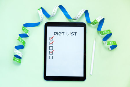 Diet list on tape measure and digital tablet on light green background.の写真素材
