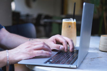 Male hands working with laptop and coffee cup on round table in outdoor cafe.の写真素材