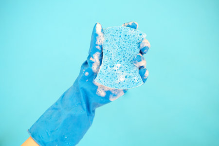 Female hand holding dishwashing sponge with foam on blue background.の写真素材