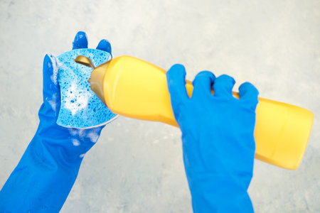 Female hand holding dishwashing sponge with foam and detergent on gray background.の写真素材