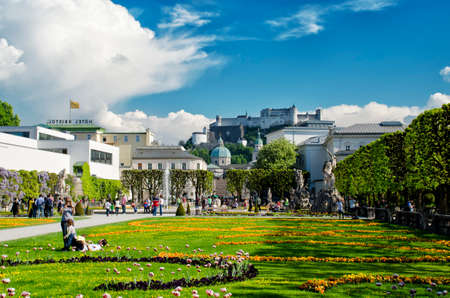 Salzburg, Austria - May 7, 2016: Beautiful view of Mirabell Gadens in Salzburg. Spring blooming flowerbeds, green trees, people walking through the alleys. Fortress Hohensalzburg in the background.のeditorial素材