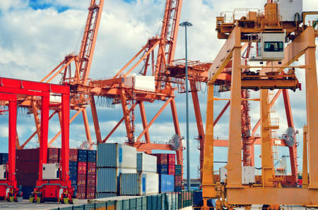 Industrial harbor, gantry cranes and container ship. Red and orange industrial cranes in port of...