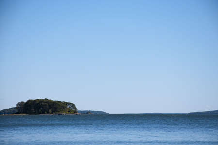 A tree-filled island in the distance with a blue sky providing copy space.の写真素材
