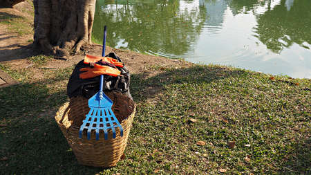 Trash bin basket , garden fork and gloves in public park. Tools for cleaning park or garden.の写真素材