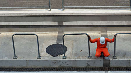 Male staff wearing orange jumpsuit and helmet for safety in racing field. Man sitting down for resting.の写真素材