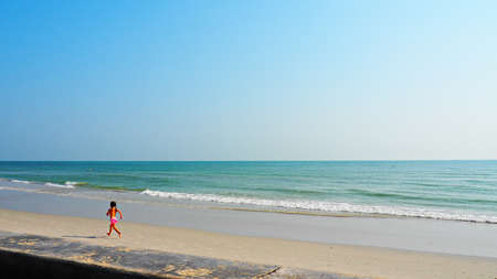 Little girl in pink swimming suit running on beach with nice blue sky and sea background. Summer holiday concept.の写真素材