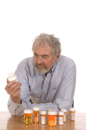 Senior man looking at prescription bottle sorting out medicine set against a white background.の写真素材