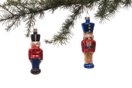 Two soldier glass ornaments hanging from a pine branch set against a white background.の写真素材