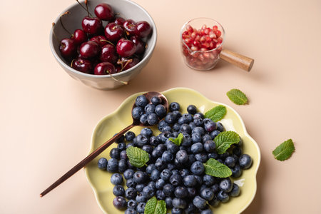 Fresh fruits in containers with mint leaves: green plate with blueberries, bowl with cherries and container with pomegranate. Healthy eating conceptの写真素材