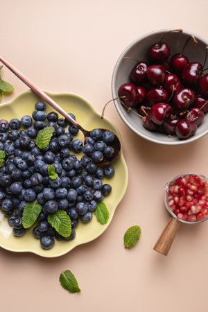 Selection of fresh fruits: blueberries, cherries and pomegranate, presented with mint leaves on beige background. Highlights freshness and vitality. Natural food conceptの写真素材