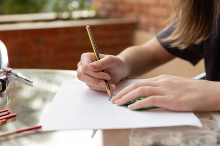 Girl's hands drawing lines with ruler and pencil on white paper, outdoor natural light. Copy space. Concept of creative learning and educational activitiesの写真素材