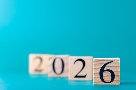 Wooden blocks with number 2026 in horizontal layout on turquoise blue background, selective focus on...