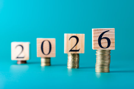 Wooden blocks forming number 2026 arranged on stacked coins, focus on number 6, horizontal image...