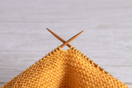 Close-up horizontal view of yellow garter stitch knitting with wooden needles inserted. Copy space....