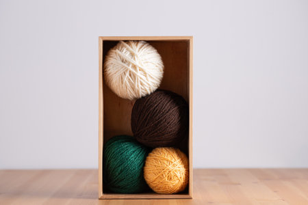 Yarn balls in neutral and green colors inside a wooden box, vertical minimalist composition on light background. Copy space. Concept of handmade craft and natural lifestyleの写真素材