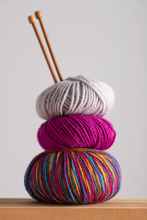 Three yarn balls stacked with knitting needles on wooden table, vertical minimalist frame with...