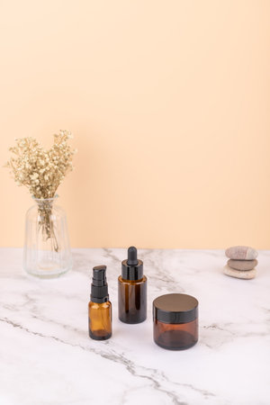 Amber bottles and cosmetic jar with zen stones and glass vase with dried flowers on marble table. Vertical image with copy space. Concept of spa decoration and natural lifestyleの写真素材