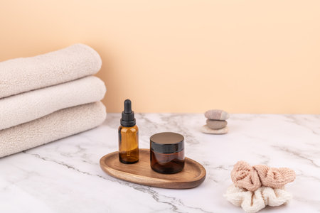 Amber dropper bottle and cosmetic jar on wooden tray with beige towels, zen stones and fabric scrunchie. Horizontal image with copy space. Concept of skincare and cozy lifestyleの写真素材