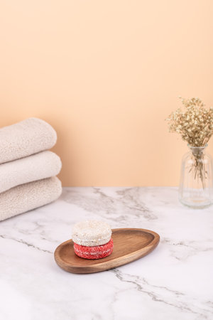 Vertical composition with natural solid shampoos on a wooden tray beside beige towels and a glass vase. Peach background and marble surface. Vertical image with copy space.の写真素材