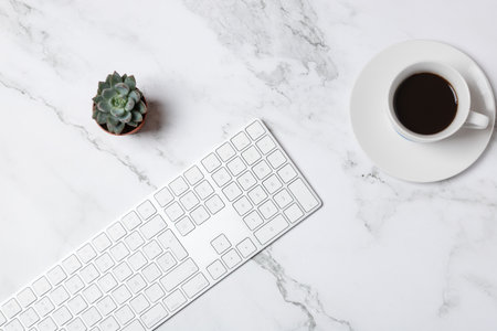 Horizontal flat lay of white keyboard, coffee cup and succulents on a marble background, clean minimalist workspace with copy space. Concept of modern workspaceの写真素材