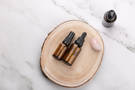 Top horizontal view of two amber glass cosmetic bottles on wooden base with rose quartz stone on light marble background. Copy space. Concept of natural skincare and wellnessの写真素材