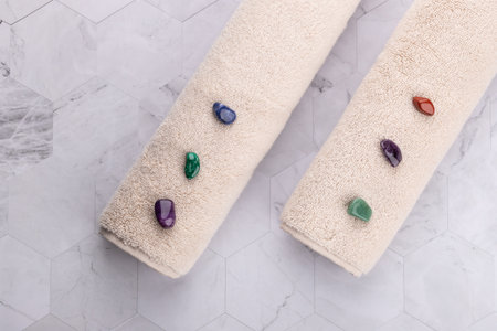 Horizontal flat lay of two beige towels with colorful decorative stones on light geometric stone...