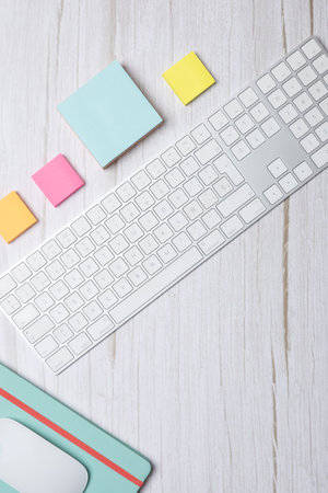 Vertical top view of a modern workspace with white keyboard, colorful sticky notes and green...