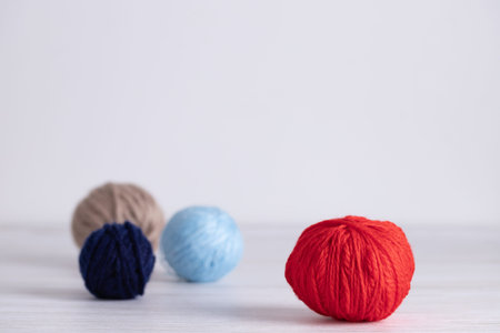 Set of yarn balls in red, light blue, beige and navy blue placed on light gray wooden surface. Horizontal minimalist image with copy space. Concept of knitting supplies